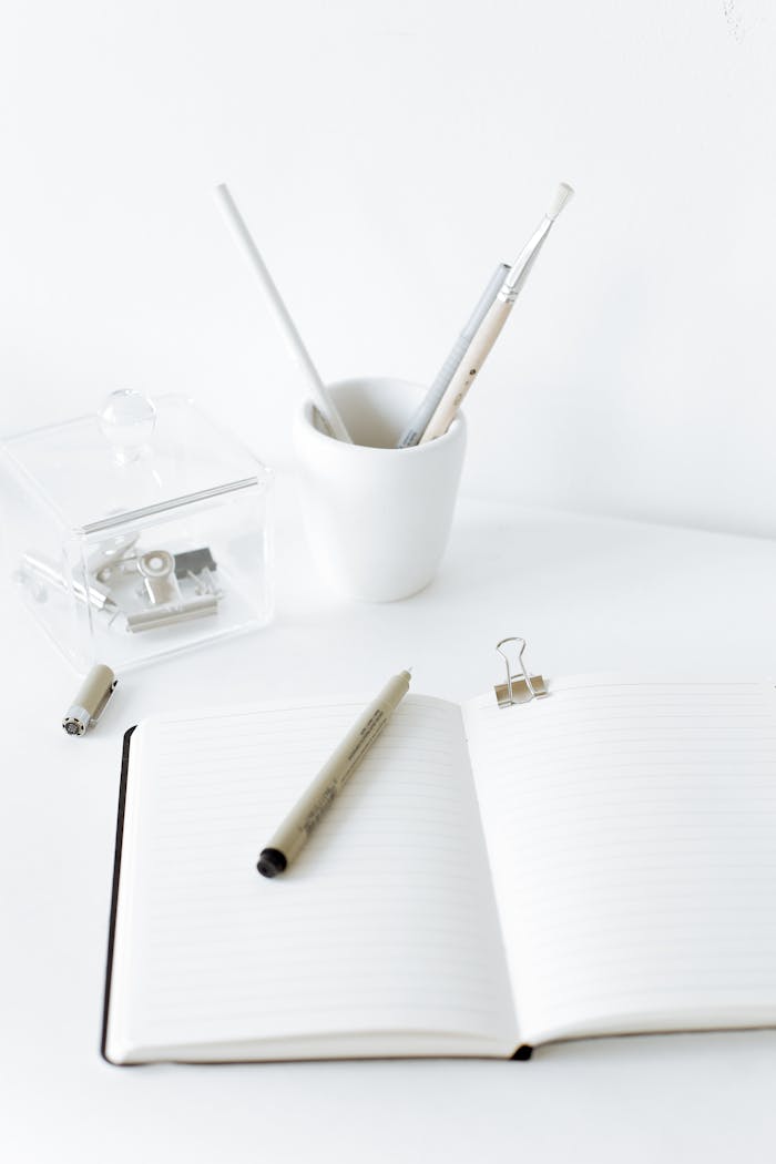 High angle comfortable workplace with opened diary with blank sheets and pen placed on white desk near pencil holder